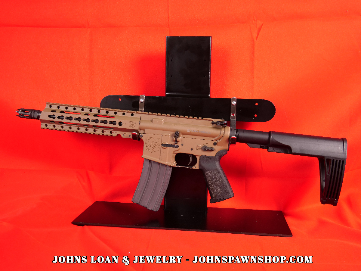 Diamondback DB15 braced AR15 pistol in FDE, chambered in .223/5.56, shown on a black table. This firearm, available from John's Loan & Jewelry, features a black pistol brace and a 30+1 magazine.