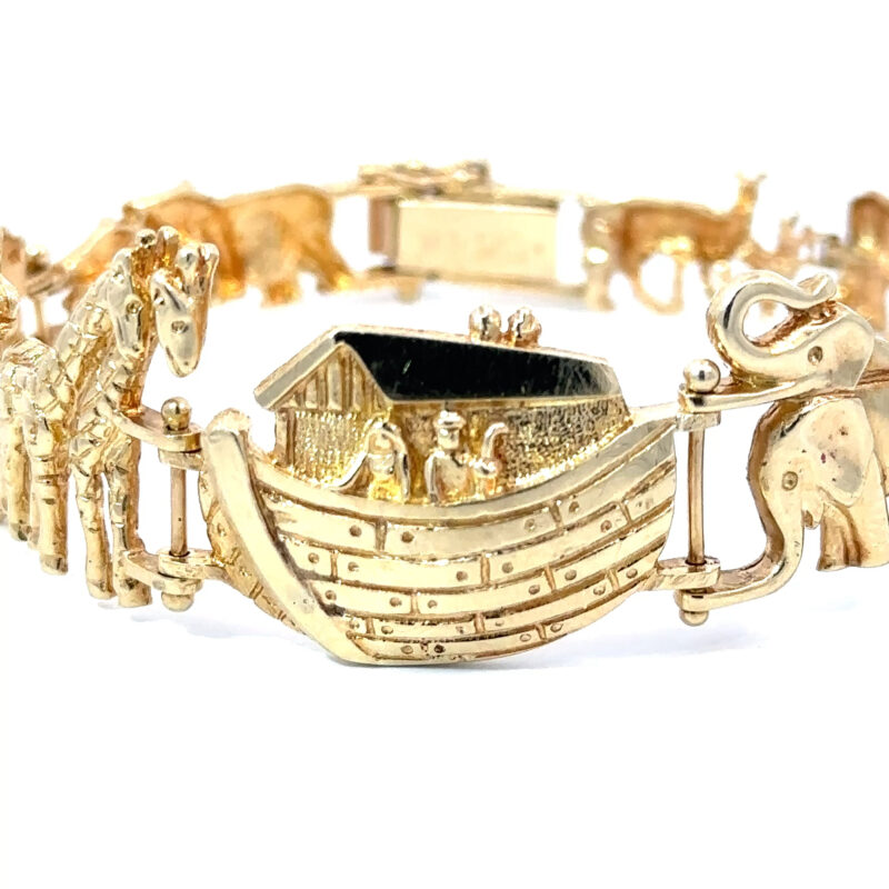 Close-up of John's Loan & Jewelry 14k yellow gold bracelet featuring Noah's Ark motif. The jewelry showcases detailed animal designs including an elephant and giraffe on a white table.