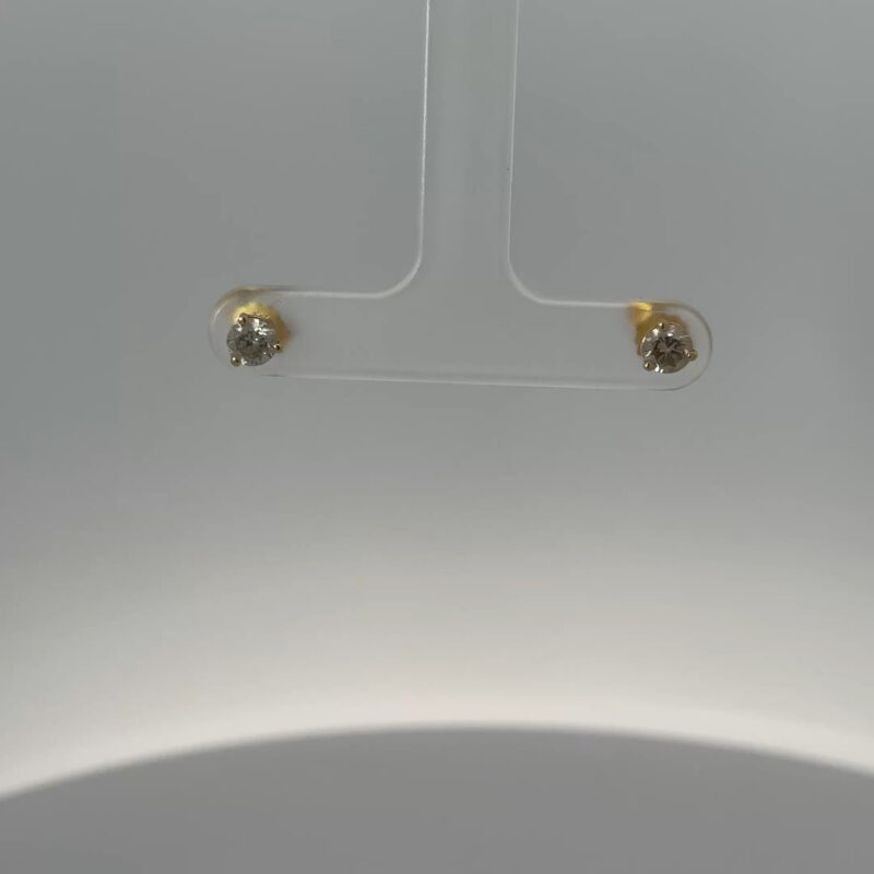 Close-up view of John's Loan & Jewelry 14kt yellow gold stud earrings, each featuring a .25ct diamond, showcased on a clear display, highlighting the jewelry's sparkle.