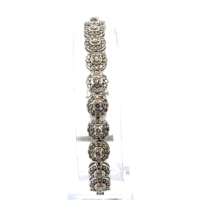 Close-up of John's Loan & Jewelry 14k white gold bracelet featuring segmented round diamond halos, displayed vertically on a clear acrylic table showcasing the jewelry's sparkle.