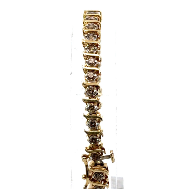 Close-up of a 14k yellow gold tennis bracelet from John's Loan & Jewelry, featuring a line of prong-set champagne diamonds. The jewelry piece is displayed on a clear acrylic table.