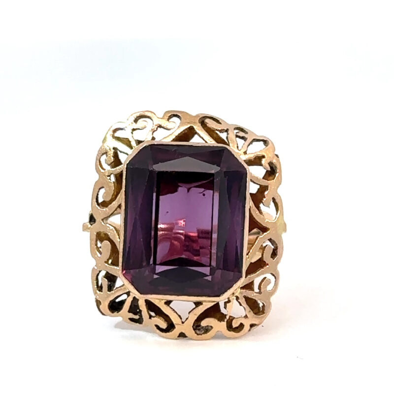 Close-up of an 18k yellow gold ring from John's Loan & Jewelry, featuring a rectangular-cut amethyst with a vibrant violet hue and intricate filigree detailing.