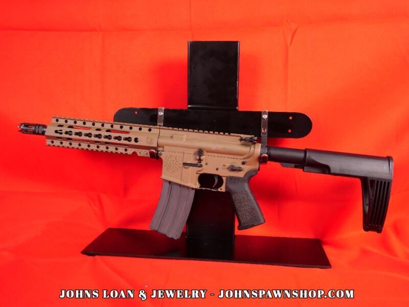 Diamondback DB15 braced AR15 pistol in FDE, chambered in .223/5.56, shown on a black table. This firearm, available from John's Loan & Jewelry, features a black pistol brace and a 30+1 magazine.