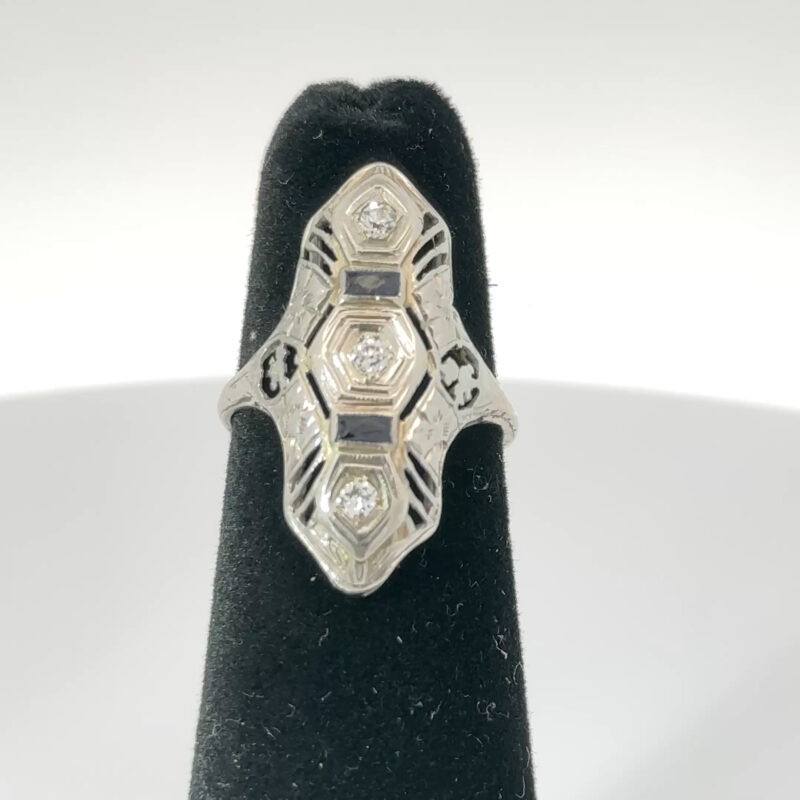 Close-up of John's Loan & Jewelry's 14k white gold ring, featuring an Art Deco design with channel-set sapphires and diamond accents, displayed on a black velvet jewelry stand.
