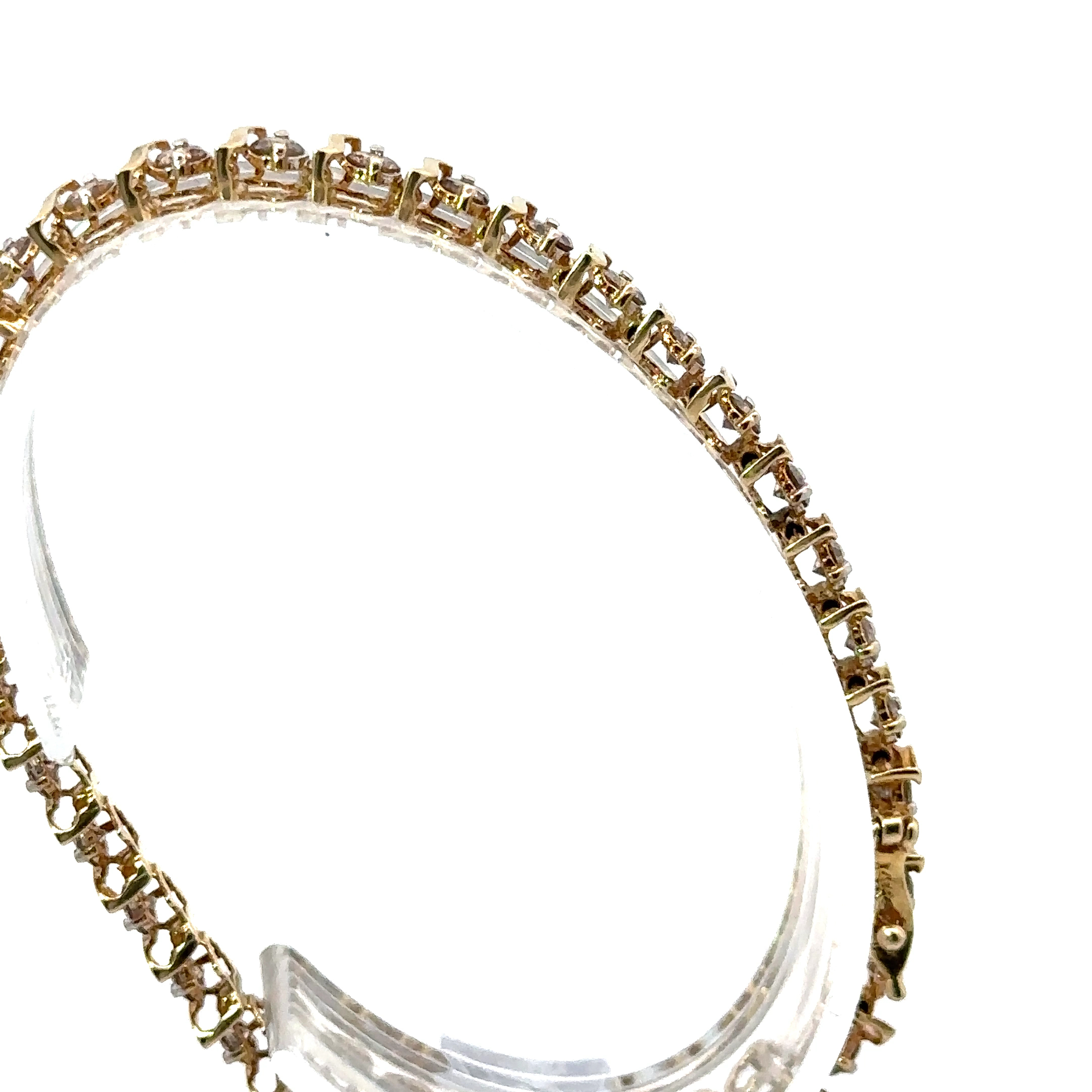 High-angle view of a 14k yellow gold tennis bracelet with champagne diamonds from John's Loan & Jewelry. The jewelry design shows individual settings, displayed on a clear acrylic table.